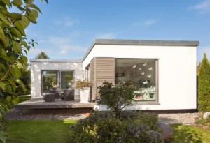 Weißer Winkelbungalow mit Flachdach, großer Fensterfront und Terrasse mit Garten