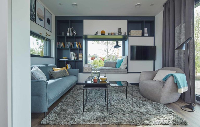 Modernes Wohnzimmer im SchwörerHaus FlyingSpace Tiny House mit großem Sitzfenster, heller Einrichtung und kompaktem Raumkonzept.