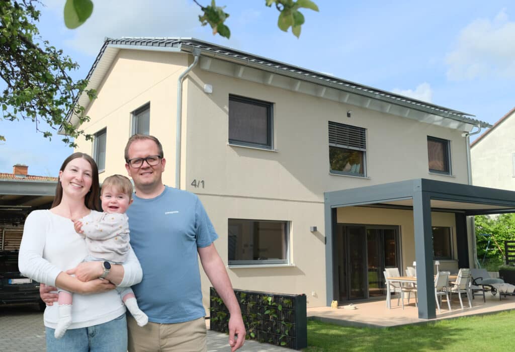 Familie vor modernem Familienhaus mit heller Putzfassade und überdachter Terrasse