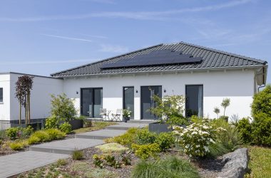 Weißes Schwörer-Haus mit Walmdach, Solarmodulen und bepflanztem Vorgarten